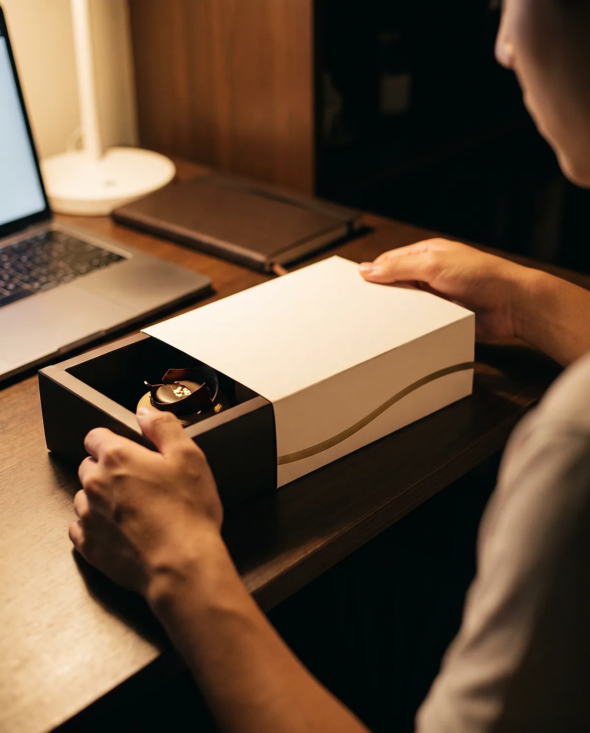 Deux mains ouvrent une boîte Misuu sur un bureau, à côté d'un ordinateur portable.