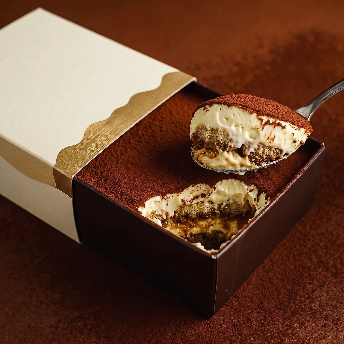 Boîte Misuu Nature ouverte, cuillère soulevant une couche de tiramisu au cacao.